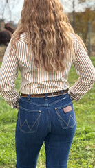 Person wearing a striped shirt and blue jeans standing in a grassy field.