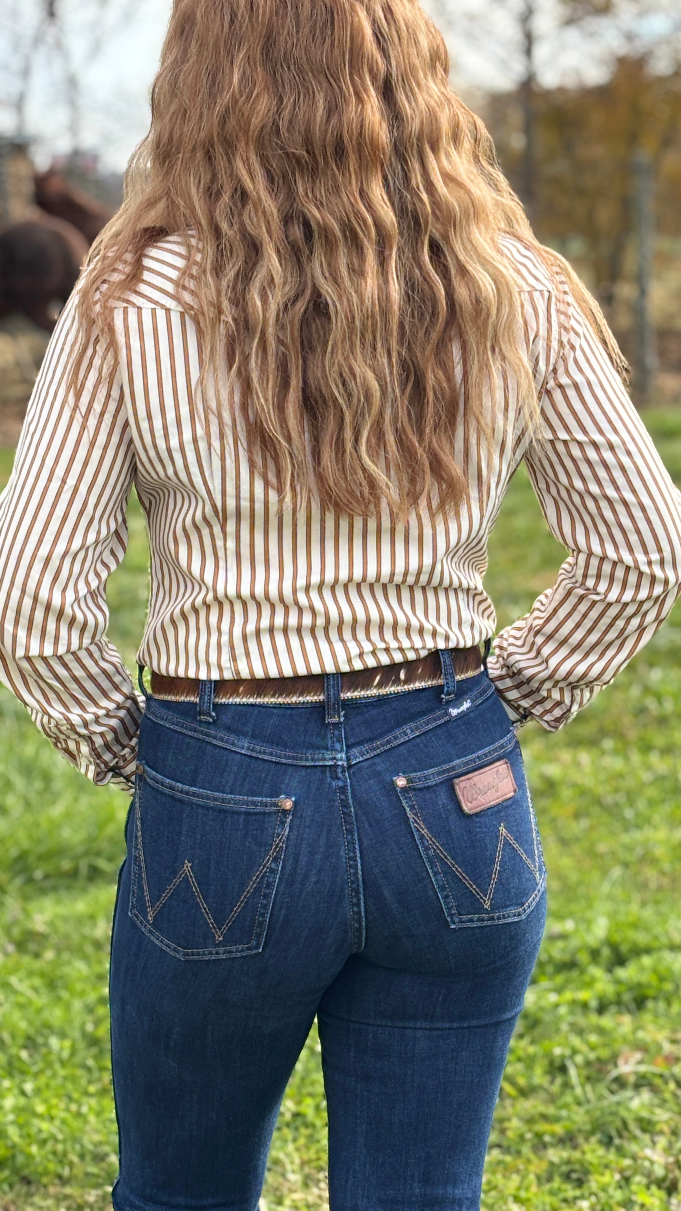 Person wearing a striped shirt and blue jeans standing in a grassy field.